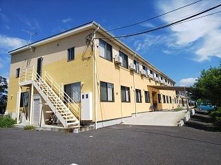 黄色と白の外壁の２階建ての建物は玄関には大きな車寄せが付き、側面の屋外階段も付いている。