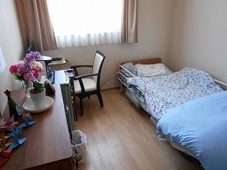寝具付きのベッドやテーブルセット、タンスなどが置かれたフローリングの部屋には大きな窓がある。