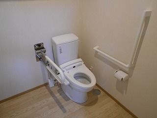 ふたのない便座が設置されたトイレは広く、壁には手すりが付いている。一つがエル字型で、一つは可動式。