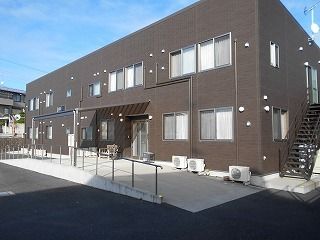 ブラウン系の建物は横に長い２階建てで玄関には手すり付きのスロープがあり、窓もたくさんついている。