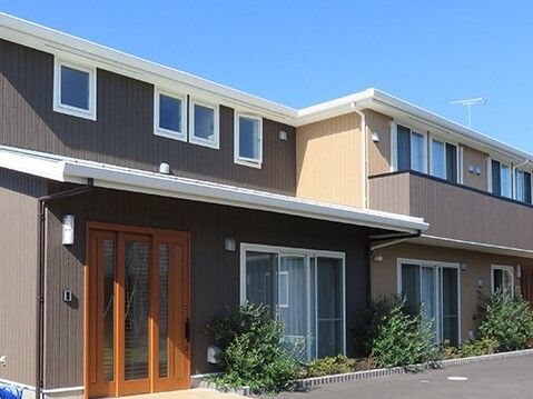 ベランダが付いた4階建ての建物の周りには草木が植えられ、敷地内はアスファルトとなっている。