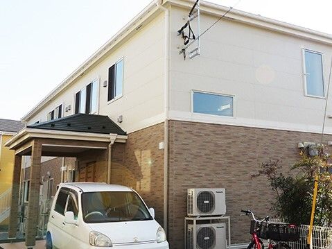 2階建ての建物。1階部分はブラウン、2階部分は白で、玄関の前には駐車場もある。