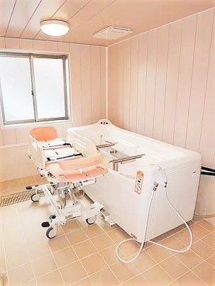 窓が付き、白とピンクの機械浴が置かれた部屋。寝たまま入浴できる設備。