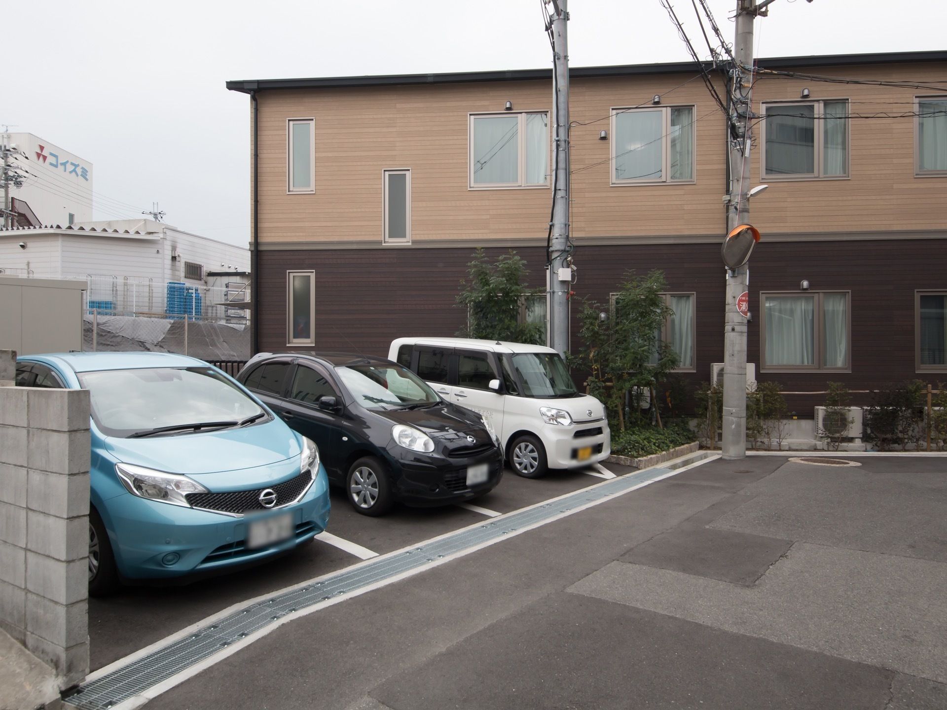 施設は2階建てで、茶色い色味の外壁で統一されている。敷地内の駐車場には、3色の車が横一列に停められている。