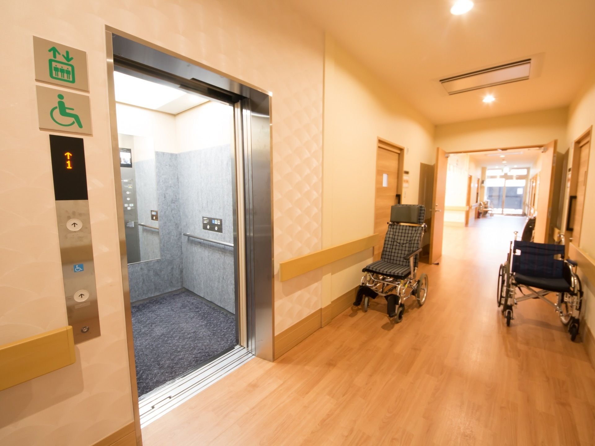 廊下は全面フローリングで、一角にはエレベーターが設置されている。壁際には、2台の車いすが置かれている。