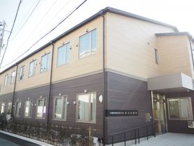 2階建ての建物。1階部分はブラウン、2階部分はベージュで、生垣もある。