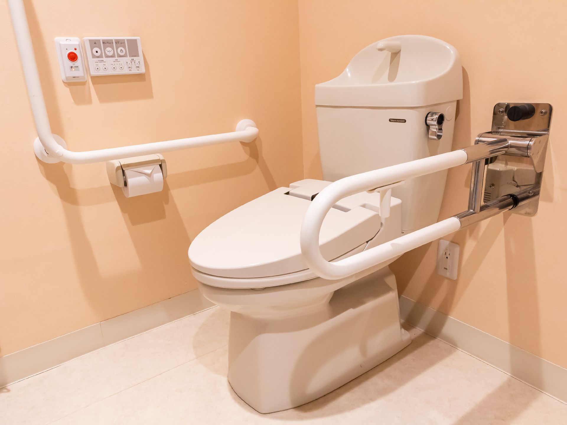 手すりが取り付けられ、隣に鏡の洗面台があるトイレ
