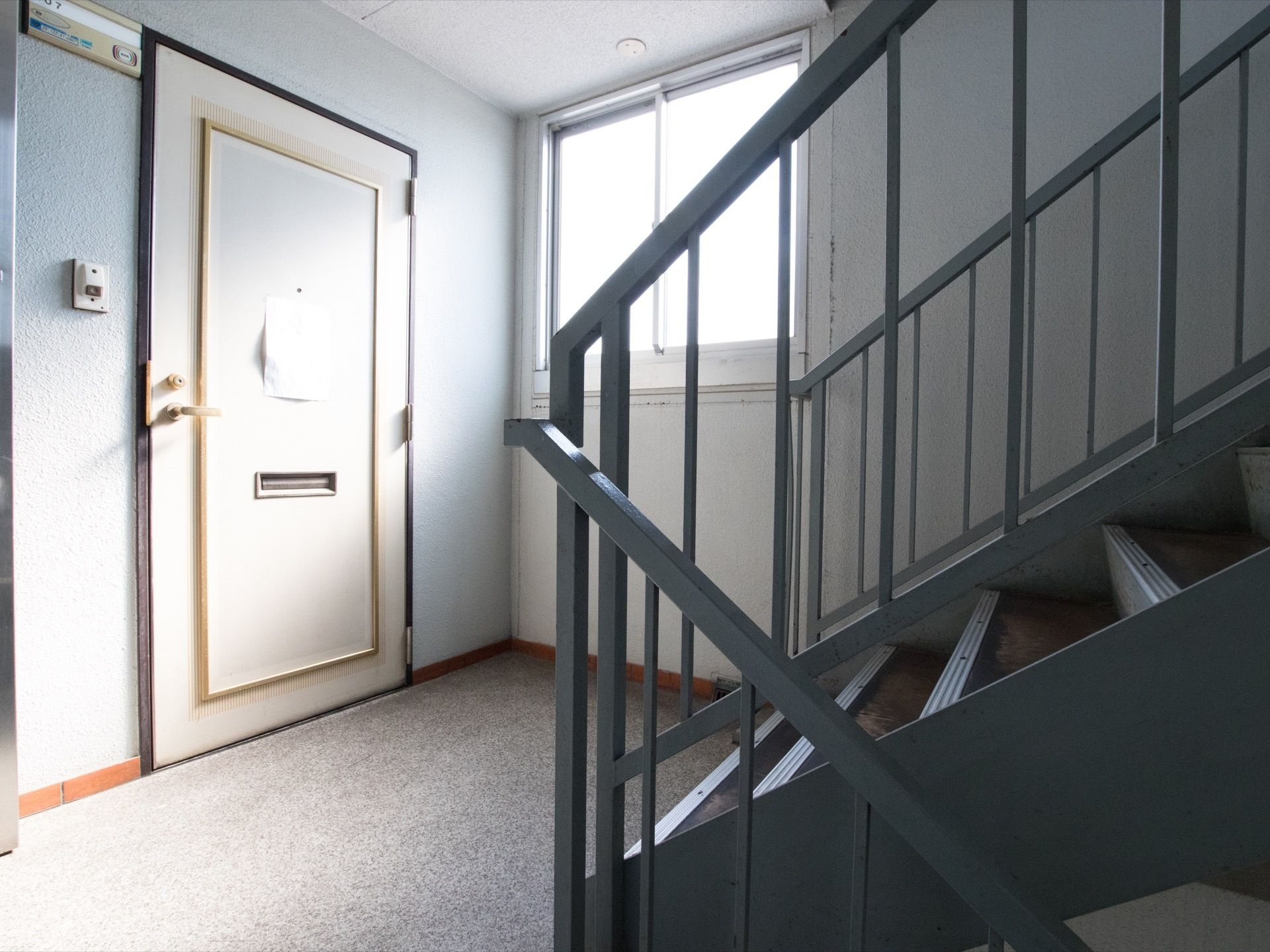 階段前にある居室の写真である。扉横の外壁には部屋番号が書かれた表札と、インターホンが設置されている。
