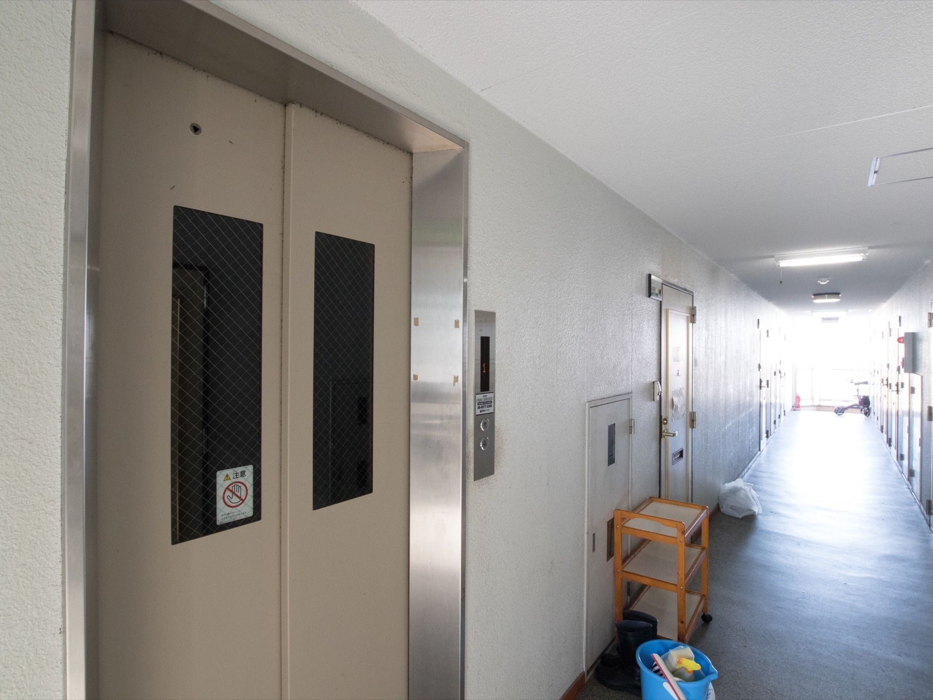 白を基調としたエレベーターの扉には、網入りのガラス窓が設置されている。横の壁には操作パネルが取りつけられている。