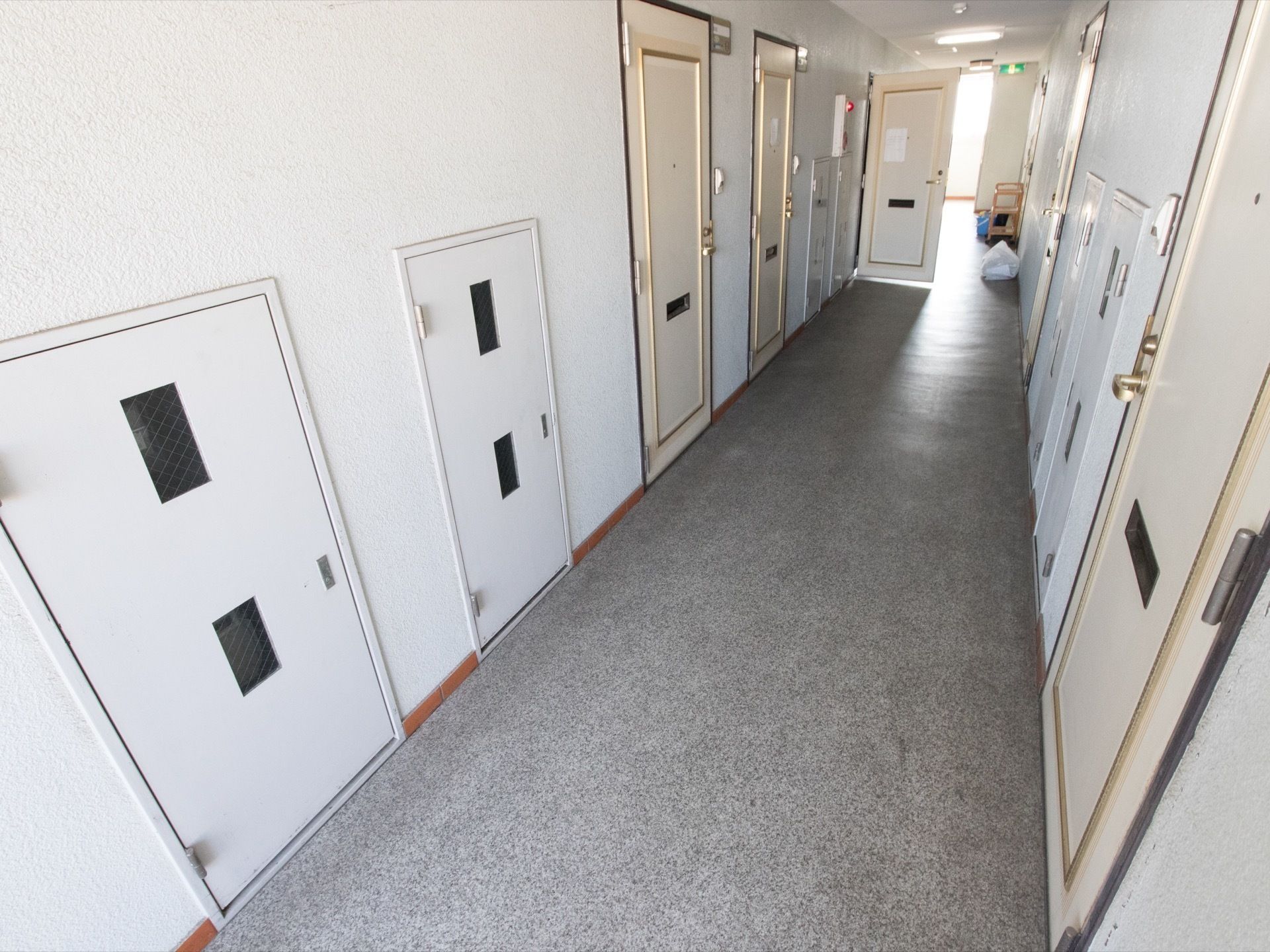 白を基調とした清潔感ある壁に、床はグレーのフローリングとなっている。廊下突き当りに非常口の看板が見える。
