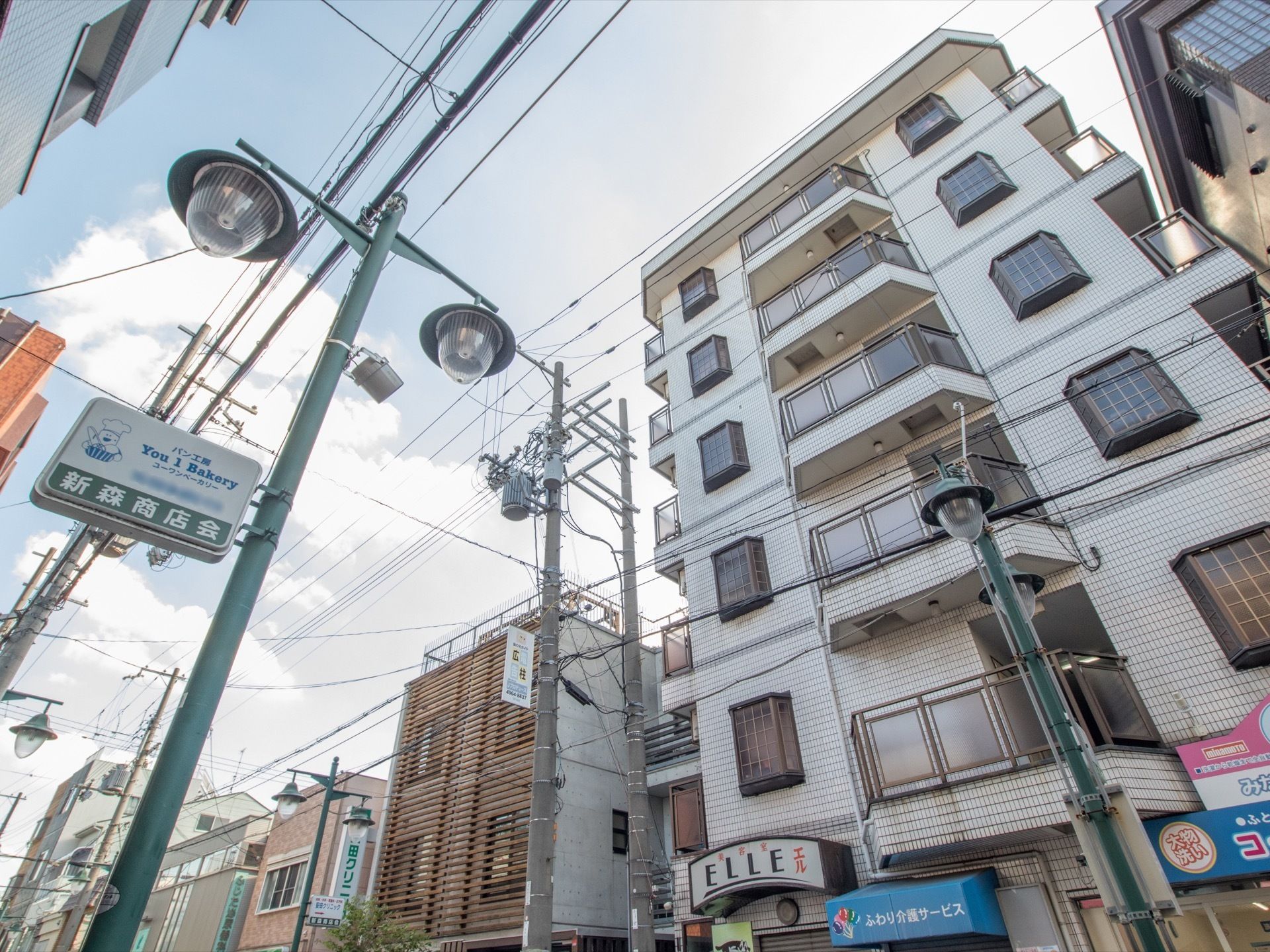 ６階建てのマンションのような外観の建物である。目の前の街灯には、ベーカリーと商店街の看板が設置されている。