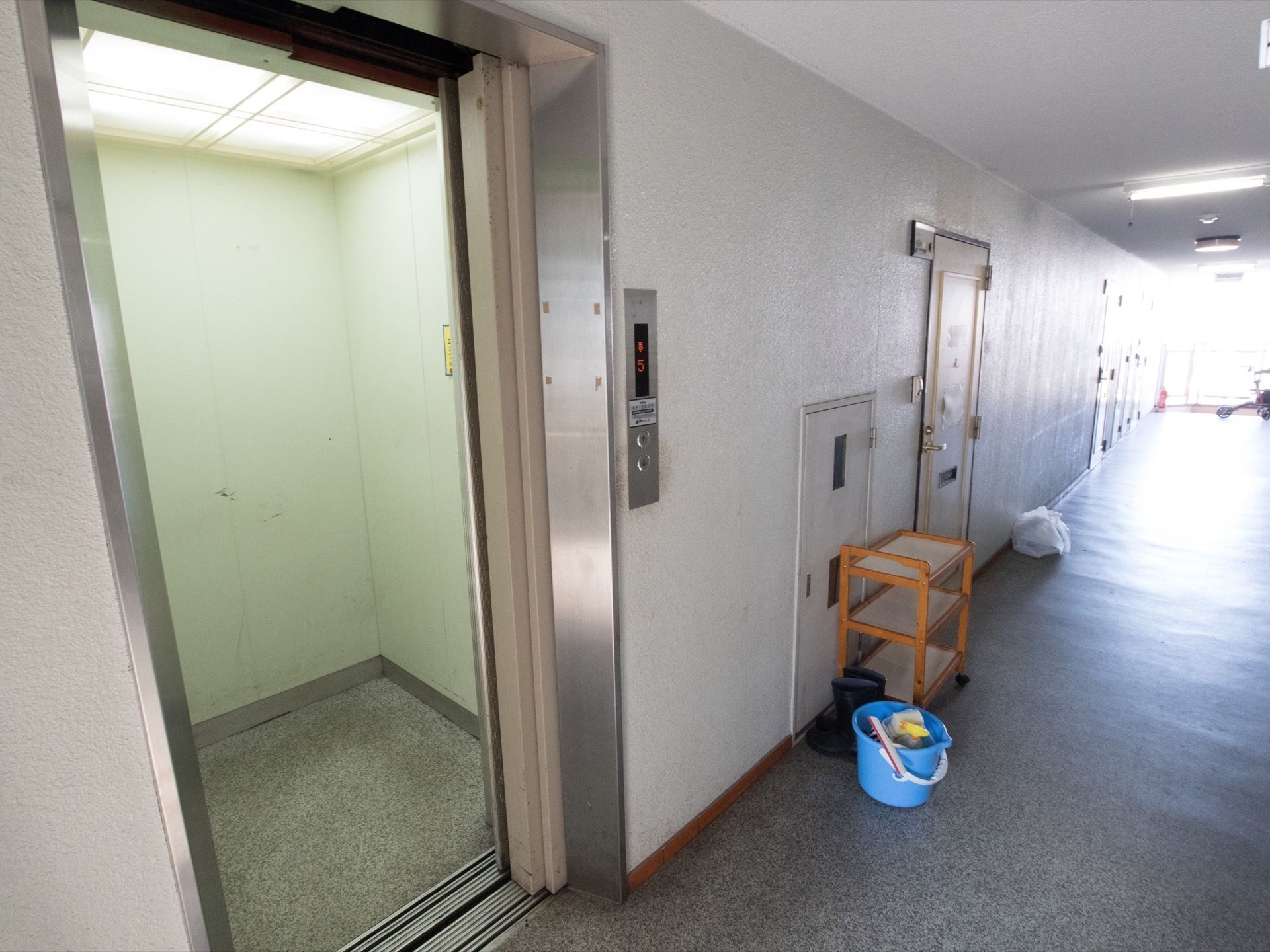 エレベーターが１基設置されており、天井部分には照明が設置されており明るい。横には掃除用具が用意されている。