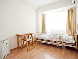 ベッドと椅子、テーブルが置いてある施設内の居室。暖房器具がある様子