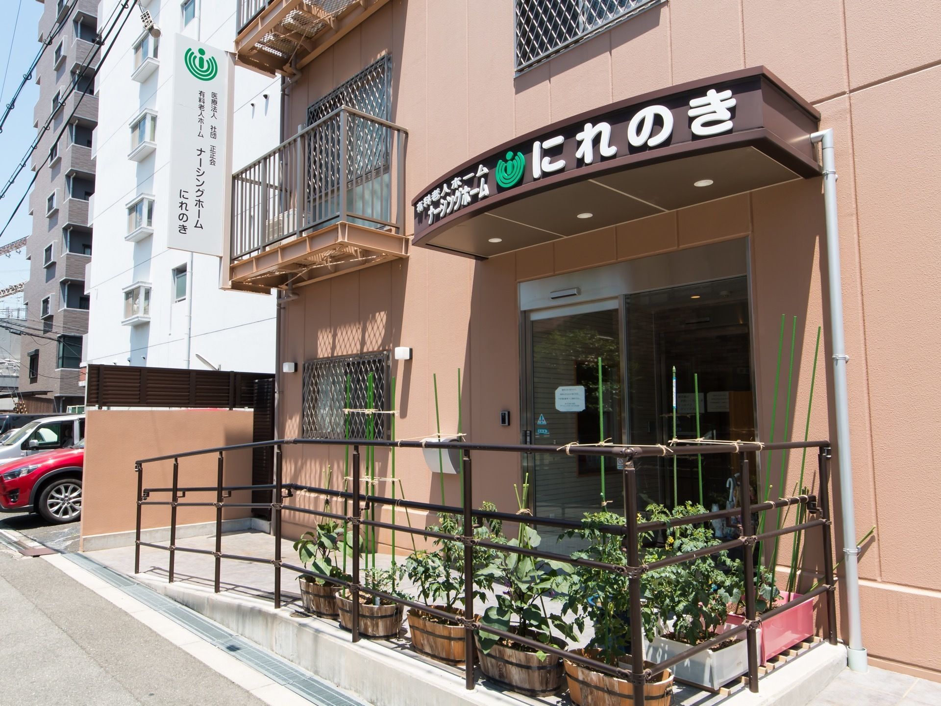 道路に面して建っている施設。玄関の屋根の部分に施設名称が明記されており、玄関前には緩やかなスロープが設置されている。