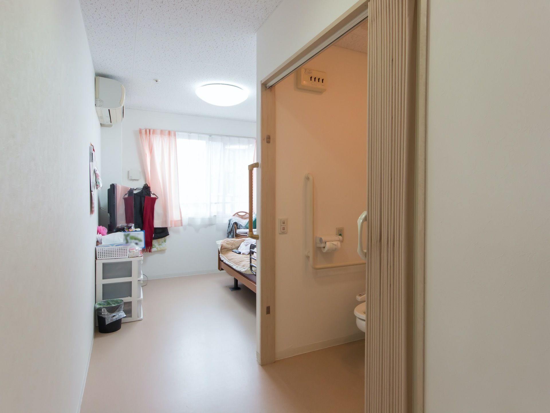 窓から陽の差し込む明るい居室にトイレが完備されている。ドアのかわりに、アコーディオンカーテンで仕切られている。
