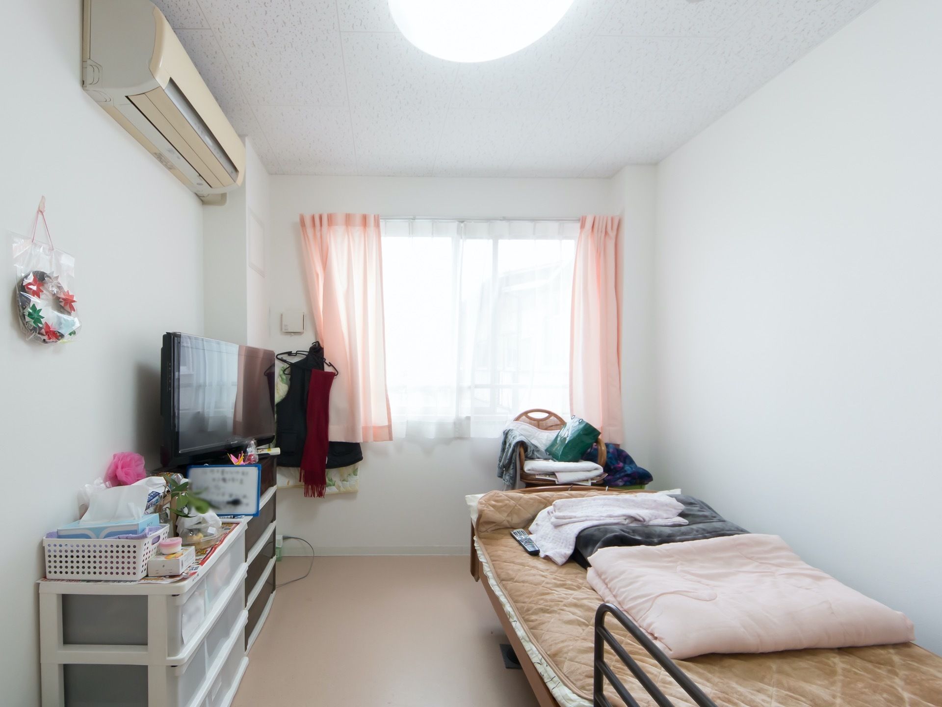 白を基調とした清潔感あふれる居室である。エアコンや介護用ベッド、液晶テレビなど、生活に必要な家具や家電がそろっている。