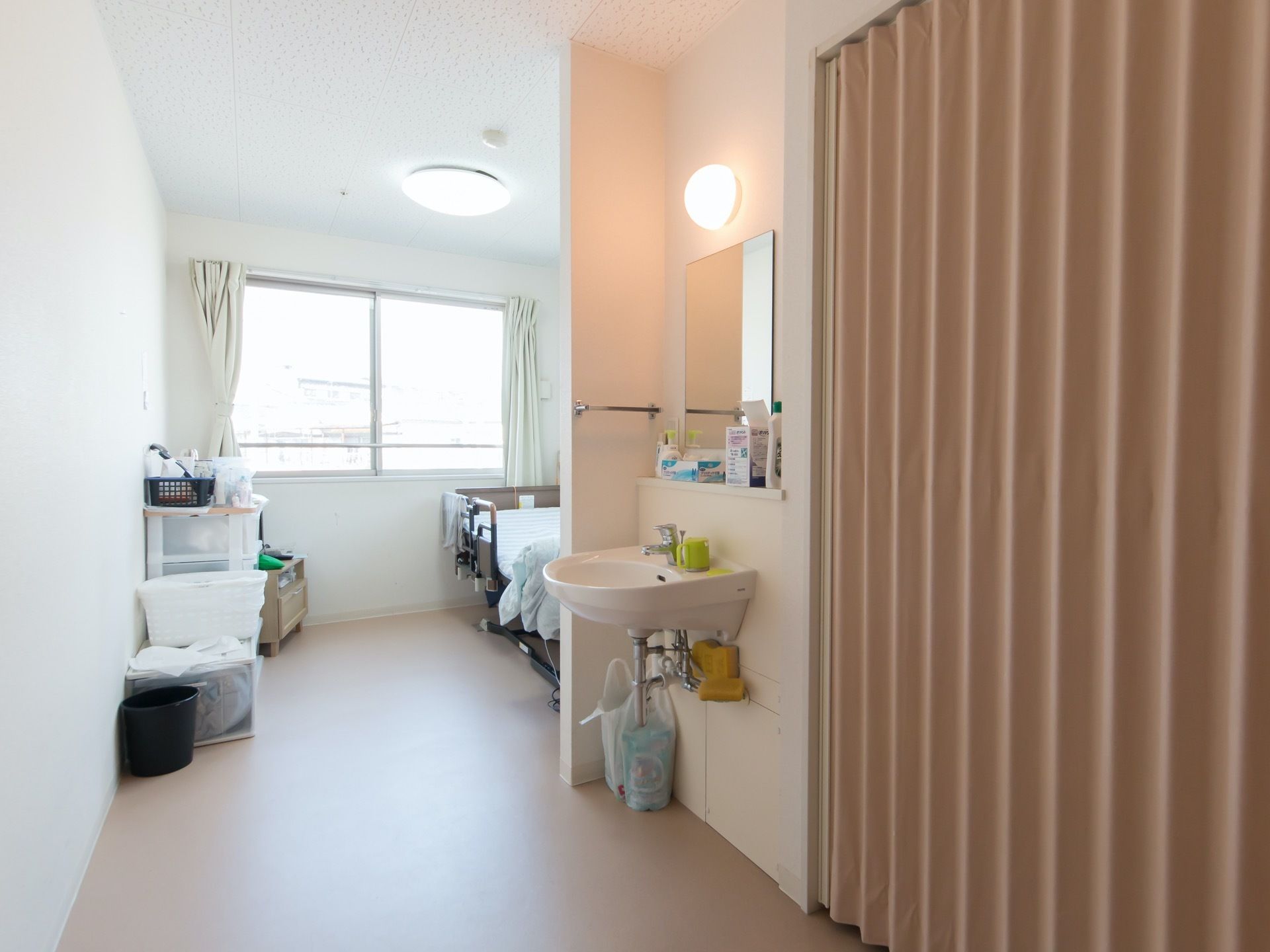 段差のないフラットな居室である。鏡付きの独立洗面台があり、奥には収納ボックスやベッドが配置されている。