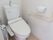 トイレ内は白色で統一され清潔感がある。動作に合わせたＬ字型の手すりが壁に設置されている。温水お尻洗浄機能がついている。