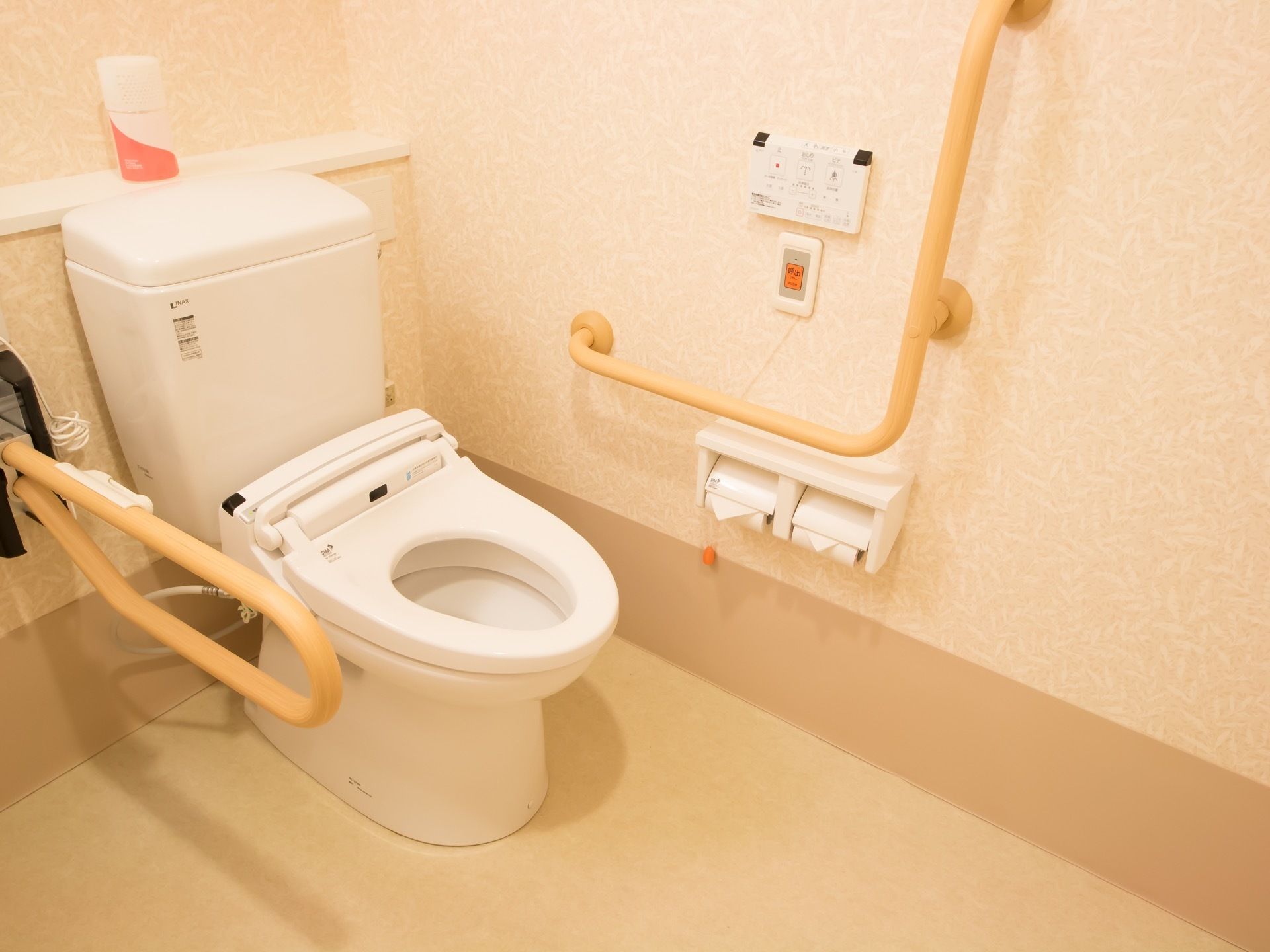 施設内のトイレは、広いスペースが確保されている。便座そばの壁には、茶色い手すりが２ヶ所設置されている。