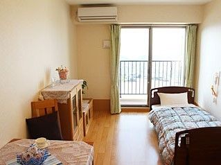 ベッド、エアコン、タンス、テーブルなどが並んでいる個室の様子