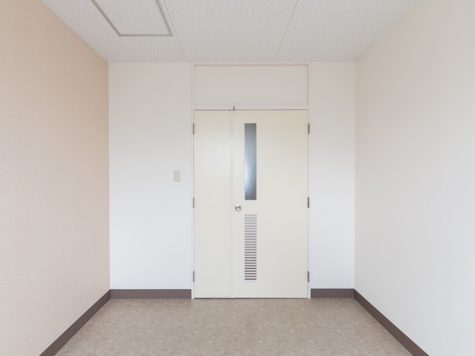 白を基調としたシンプルな居室。床はベージュのシート張りになっている。正面に両開きで大きく開口できるドアが付けられている。
