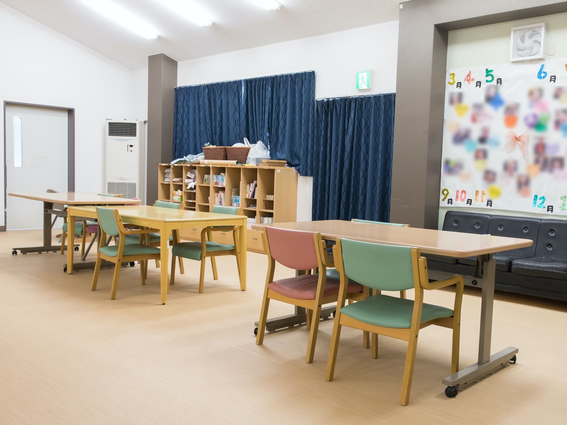 ダイニングテーブルが３台あり、それぞれ椅子が配置されている。右側の壁は窓になっており、一部に掲示スペースが設けられている。