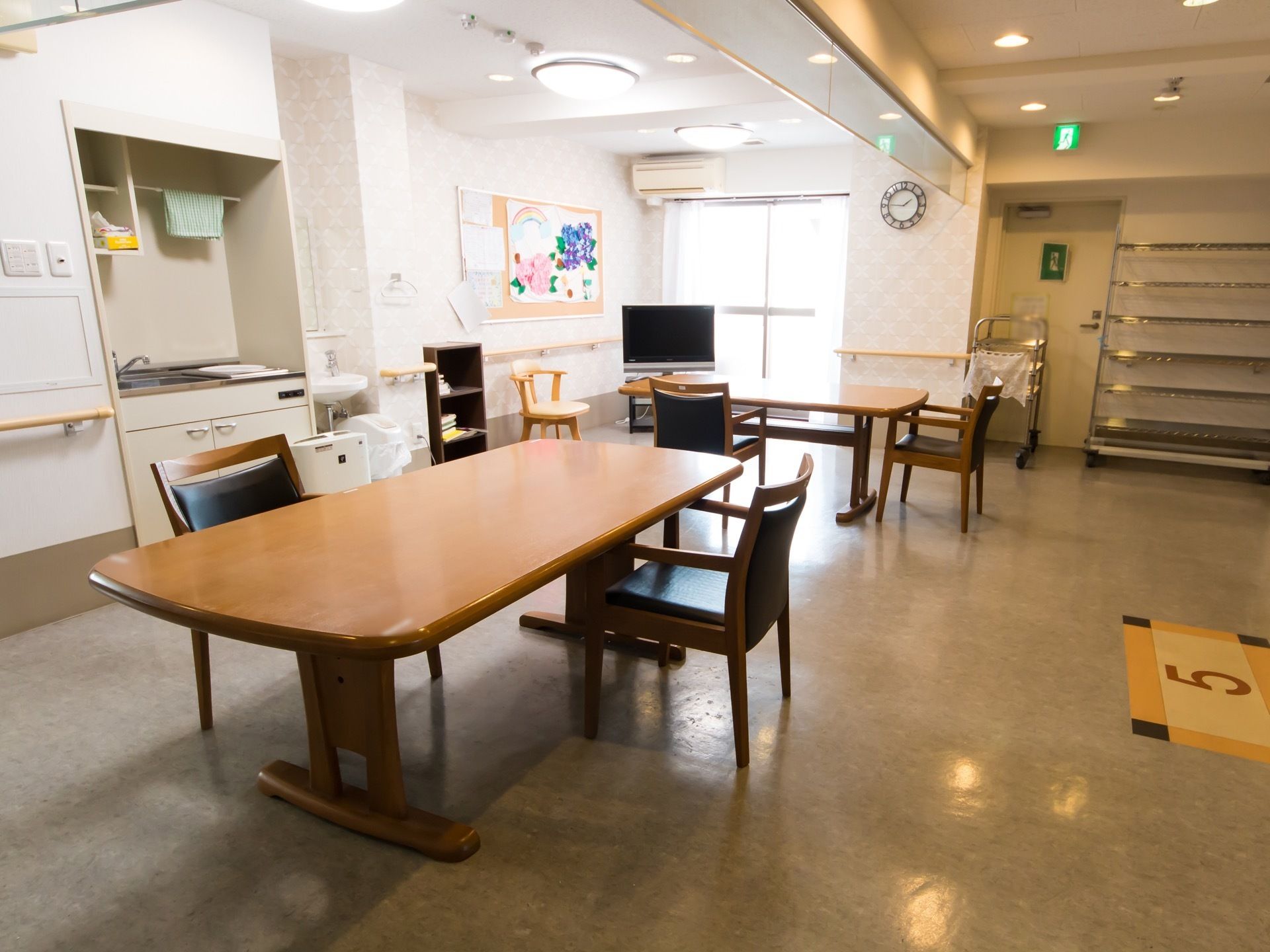食堂の床には階数が書かれており、木目調のテーブルと黒い椅子が置かれている。左側にはミニキッチンや洗面台が設置されている。