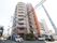 茶色とベージュの外壁になった高い建物があり、右側には外階段が付いている。建物の横には駐車場があり、車が3台停められている。