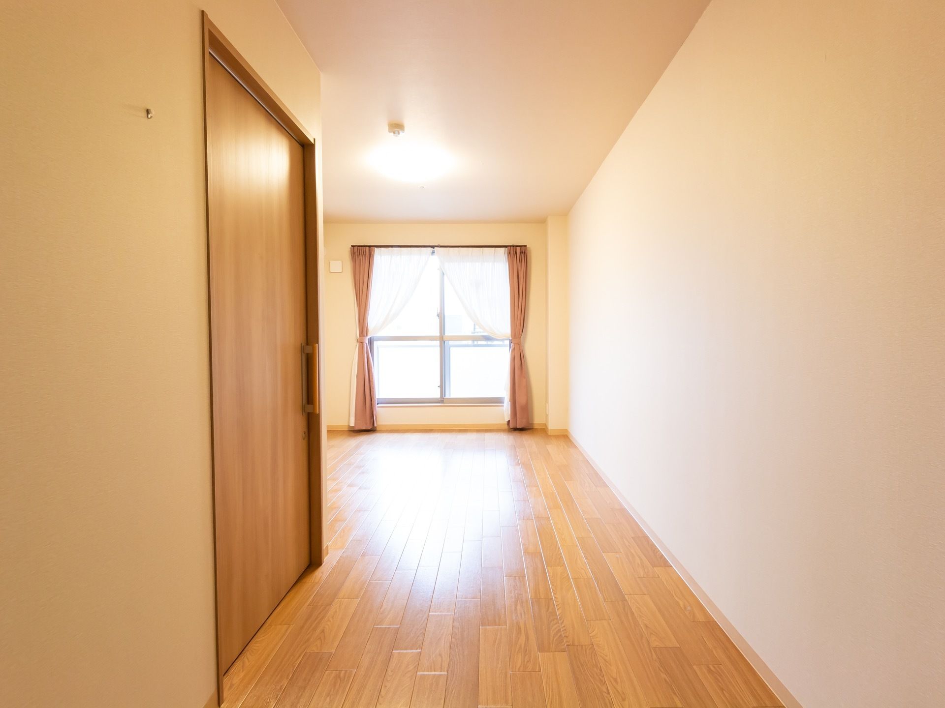 居室は廊下が広く設計されており、奥には大きく縁取られた窓がある。カーテンがまとめられ、あたたかい日の光が差込む。