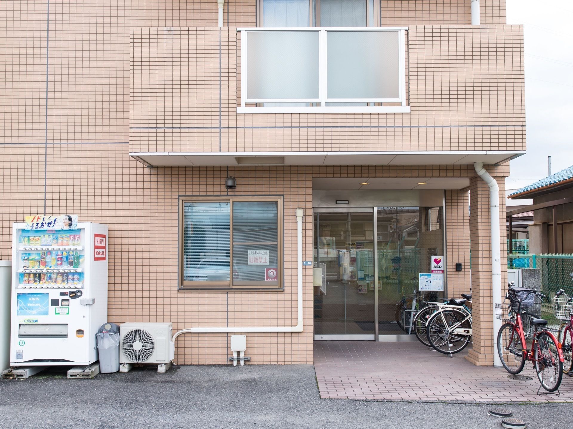 自動ドアの玄関があり、入り口付近には自転車が数台停められている。建物の壁際には自動販売機が設置されている。