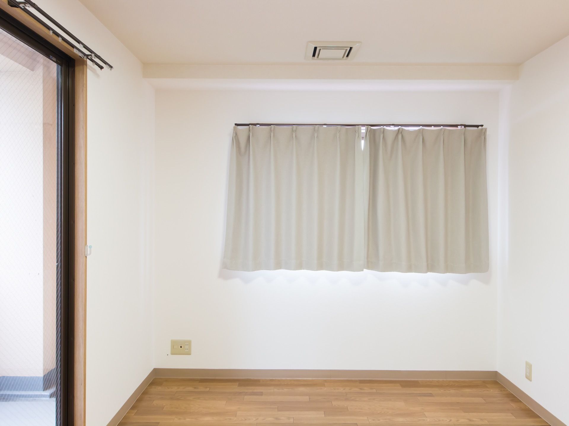 白い壁にフローリングの居室。角部屋で、横はバルコニーに出られる掃き出し窓があり、正面には胸の高さあたりに窓が付いている。