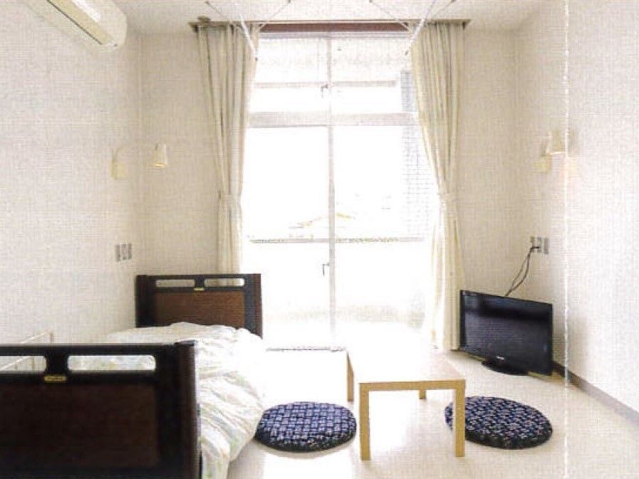 白を基調とした居室には、ベッドやエアコン、テーブルに座布団、そしてテレビ化置かれている。