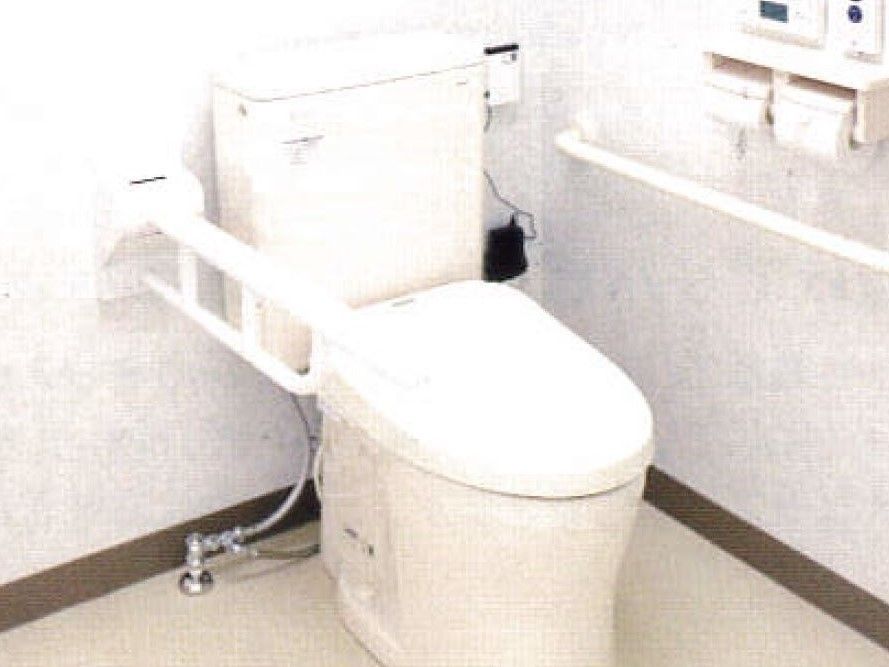 白いトイレの両サイドに手すりが付き、トイレットペーパーホルダーの上には呼び出しボタンがある。