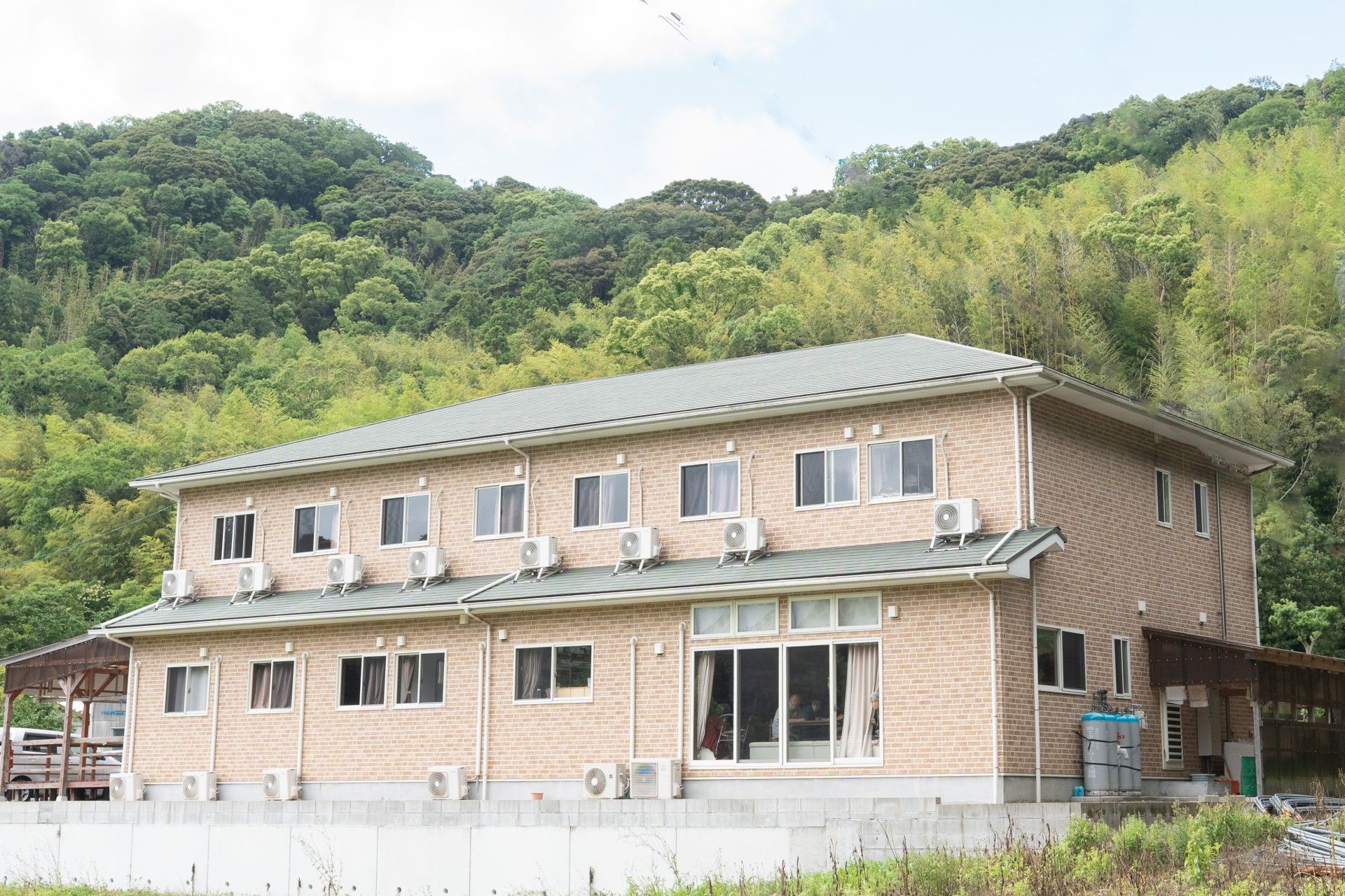 2階建ての建物はブラウン系で玄関前にスロープが、また屋外に避難用の階段もある。