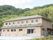 2階建ての建物はブラウン系で玄関前にスロープが、また屋外に避難用の階段もある。