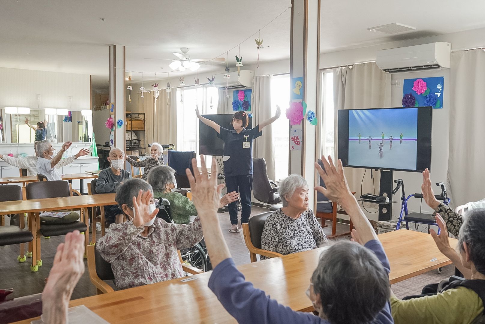笑顔で話をしている女性と高齢夫婦が日当たりのいい芝生の上に並んで座っている。