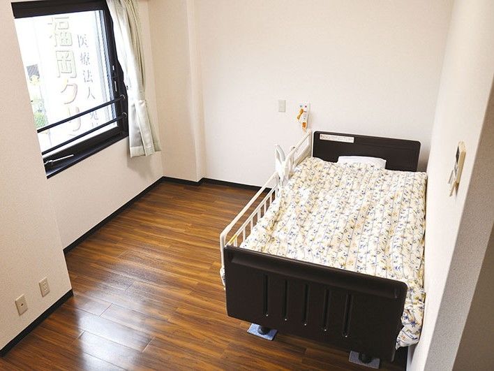 一人用の介護ベッドが置いてある小さなワンルームタイプの部屋。窓がありカーテンがかかっている様子
