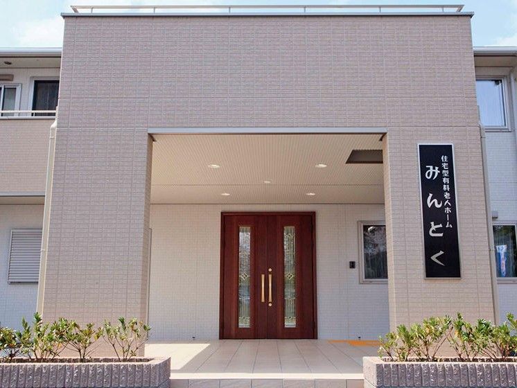 外観の玄関付近のアップ。ベージュ外壁にホームの看板が掲げられている。