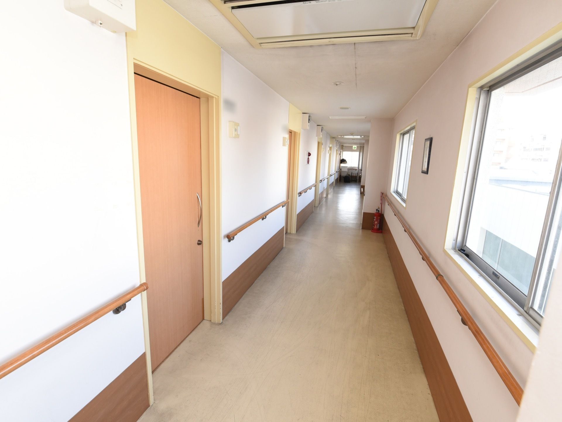 白い壁の下部分に茶色いラインがついた廊下である。窓が等間隔でついているので、日中は自然光だけで明るく過ごせる。