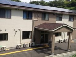 車寄せが付いた玄関が中央にある2階建ての建物。周辺に緑が多い。