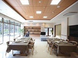 ブラウン系の色でまとめられた落ち着いた雰囲気の食堂。テーブルクロスがセットされたテーブルが二つ並び、奥にはテレビも置かれている。