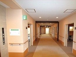 両サイドに手すりと居室が設置された廊下。白い壁に木目調の手すりがよく目立つ。