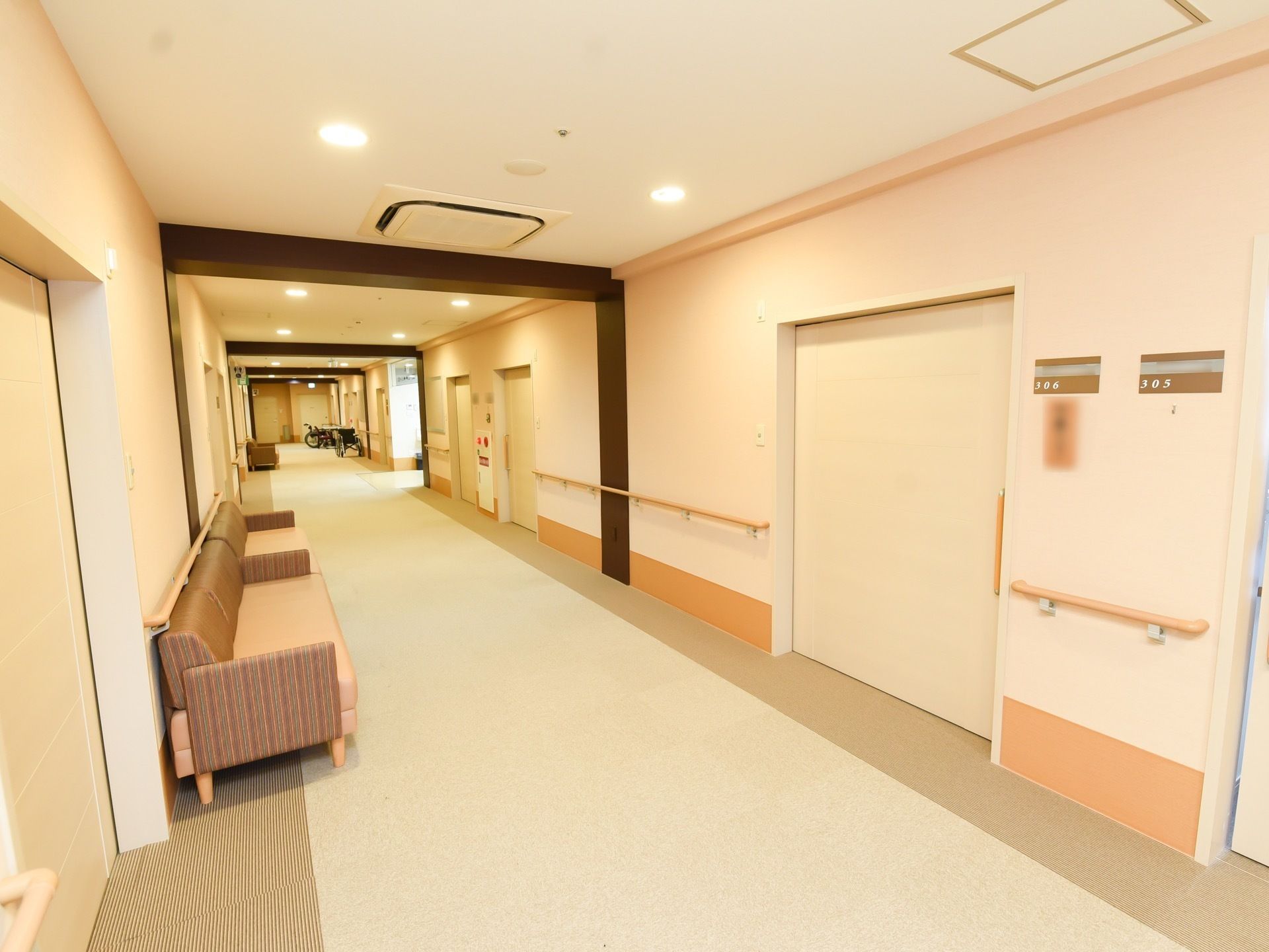 明るい色合いの通路に、茶色の枠がアクセントになった通路である。壁側にソファが設置されている。手すりもある。