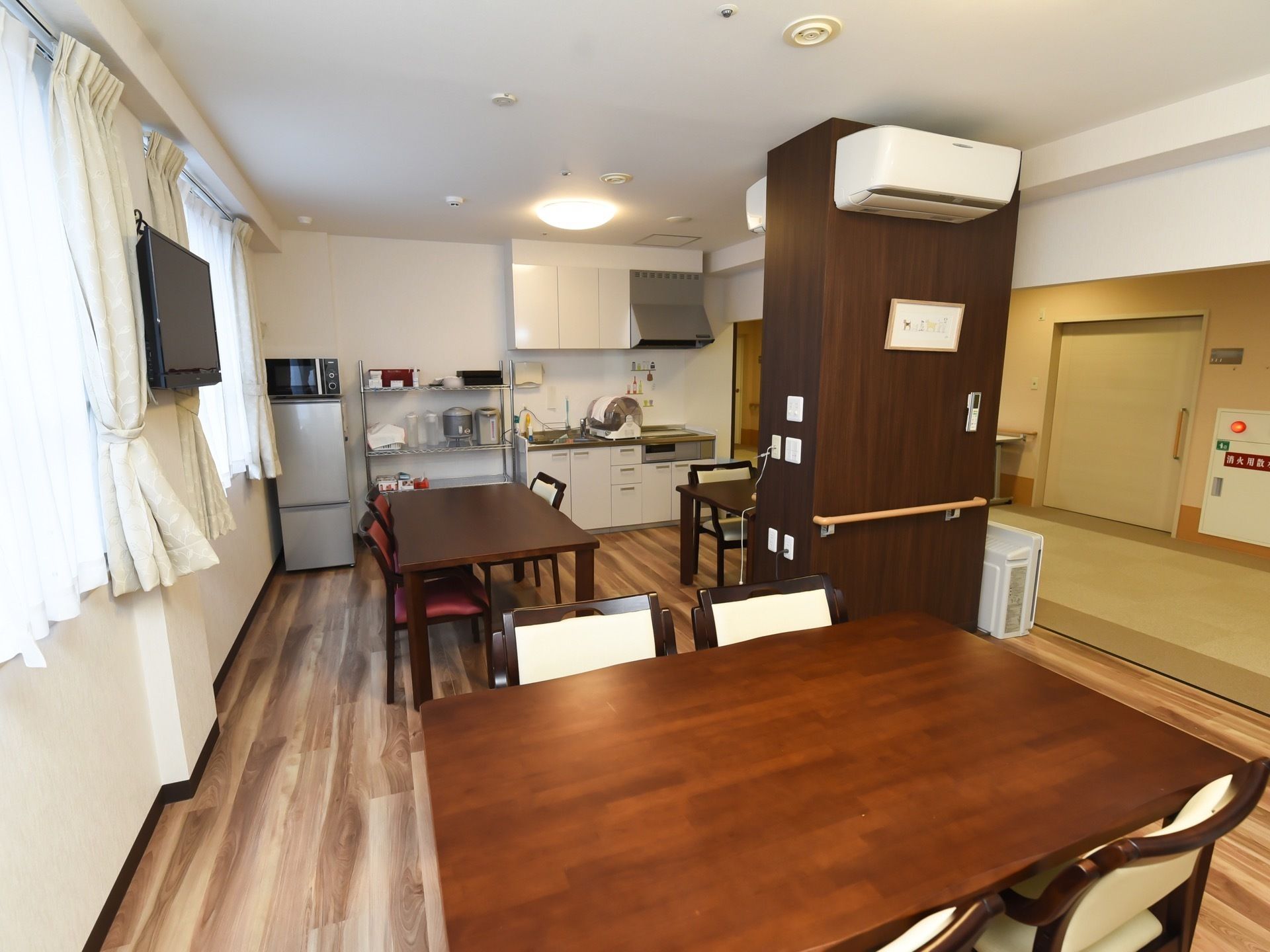 床材は木を使用した、フローリングである。広々としたテーブルに、茶色と白色の椅子がセットされている。壁かけのテレビもある。