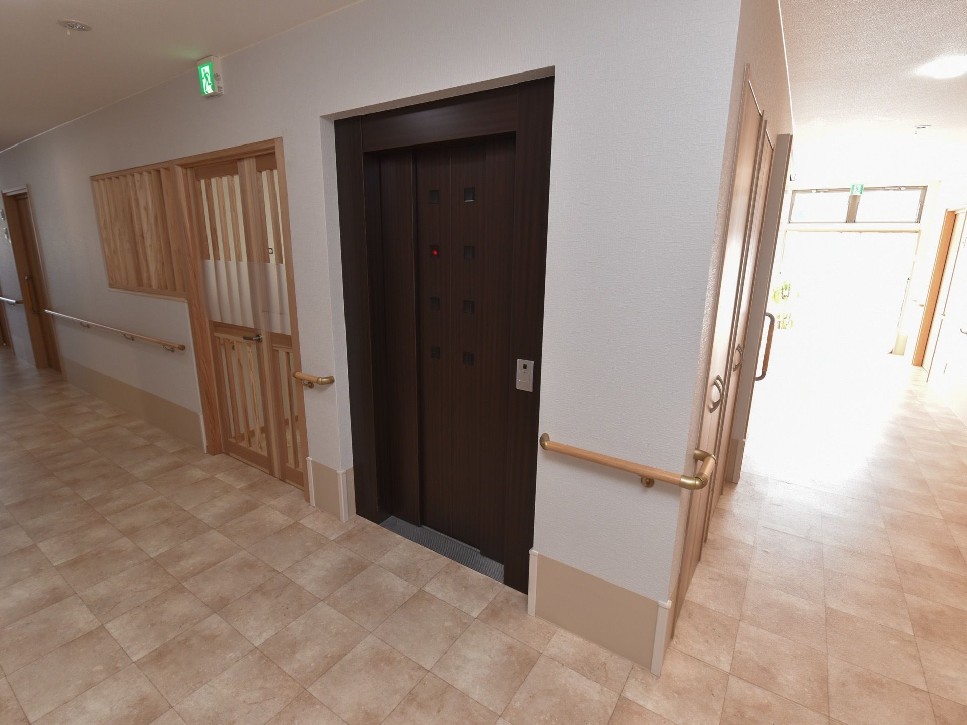 明るい廊下の壁には手すりが設置されている。体を支えながら安全に移動することができる。ダークブラウン色の扉のエレベーターがある。