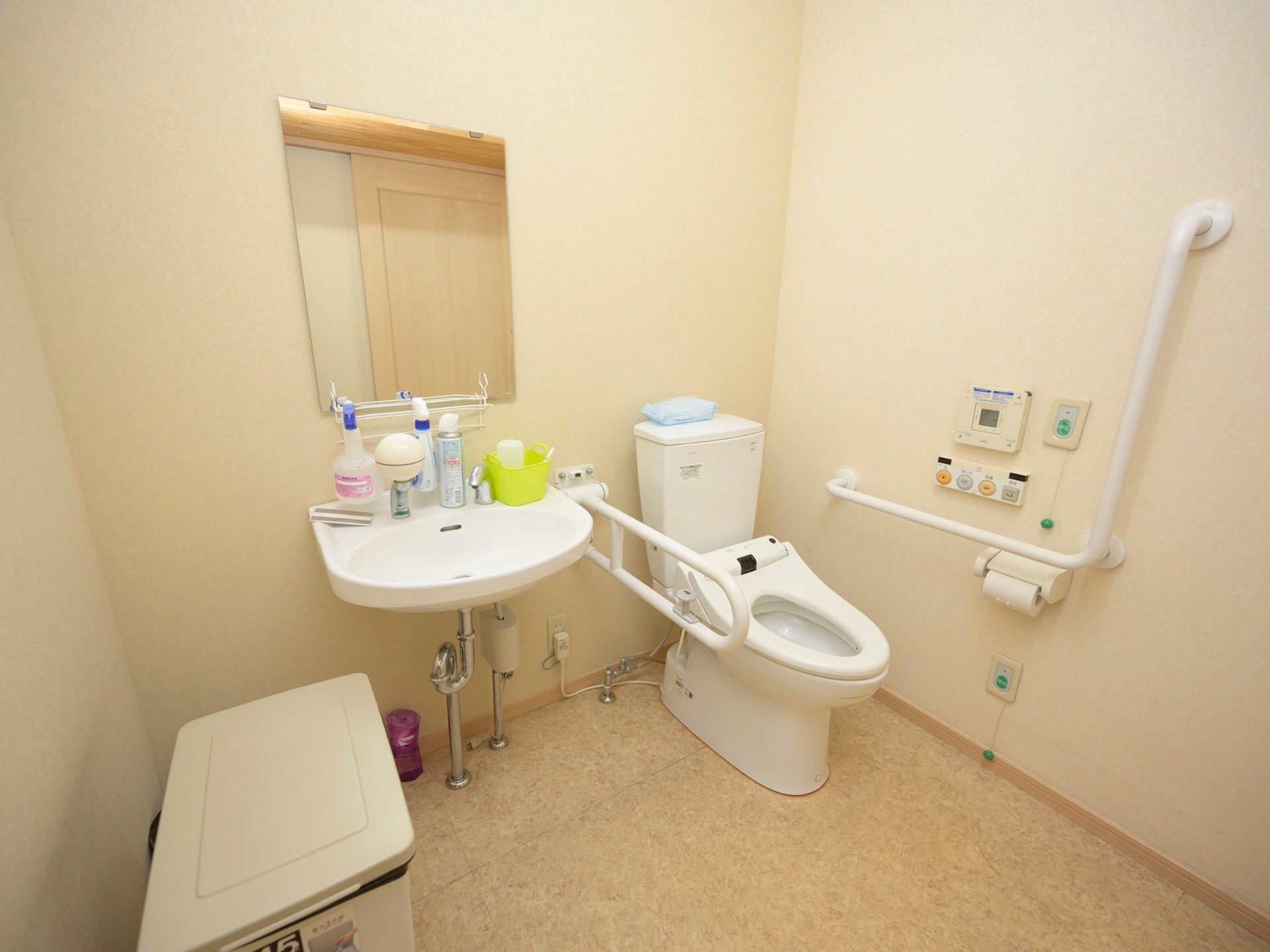 温水洗浄便座器が完備されているトイレである。壁には、L字型手すりや緊急呼び出しブザーが上下2段に設置されている。