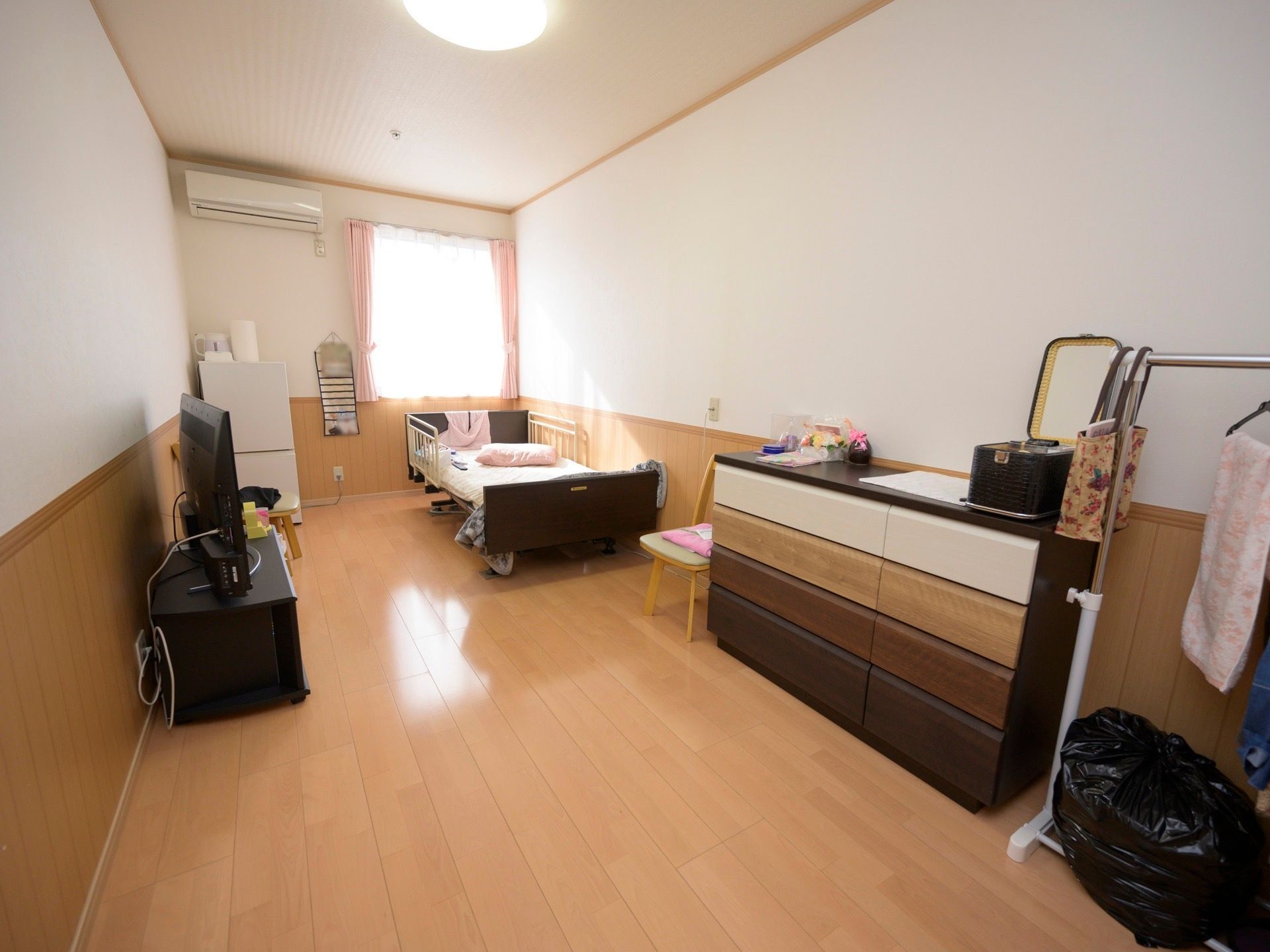 窓やエアコンが設置された居室である。カーテンが引かれ介護用ベッドがある。入居者様のお好みにデザインされている。