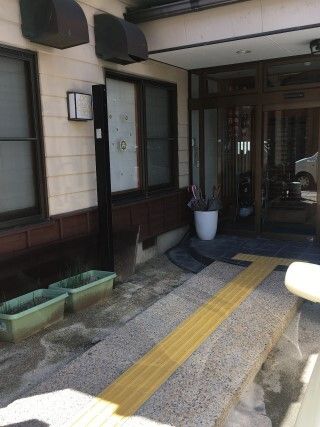 点字ブロックが敷かれた玄関のアプローチ。端にはライトグリーンのプランターが複数置かれている。