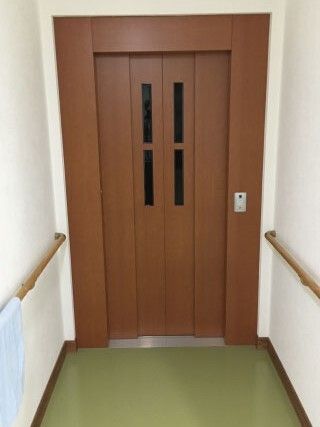 ブラウンの扉が設置されたエレベーター。両サイドに手すりがあり、シンプルな操作ボタンがついている。