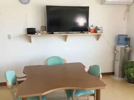 グリーンの椅子がセットされたダイニングテーブルは凹凸があるデザインで、壁にはテレビが設置されている。
